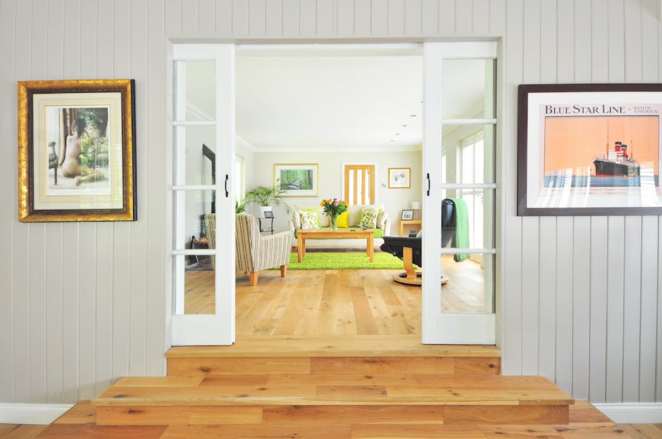 A bright, spacious entrance hall of a home featuring a white front door with a rectangular window at the top, flanked by two large double-hung windows with white trim allowing natural light to illumin